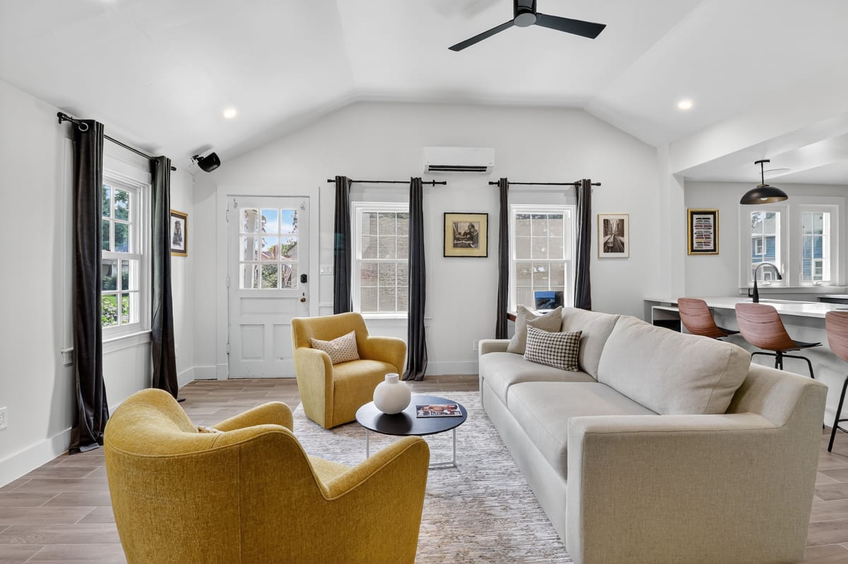 Living room with two mustard swivel chairs, a long cream sofa and black drapery under a vaulted white ceiling.