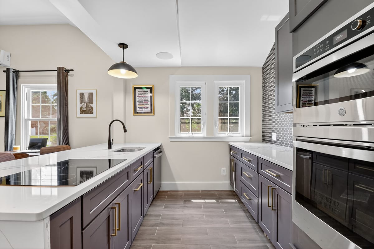 The finished galley kitchen with grey-brown cabinetry, brass pulls, a white quartz counter, a black faucet and a stainless wall oven.