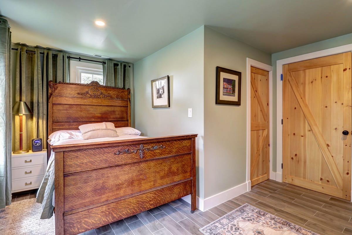The bedroom from the doorway, with the antique bed, sage curtains and a framed print above the nightstand.