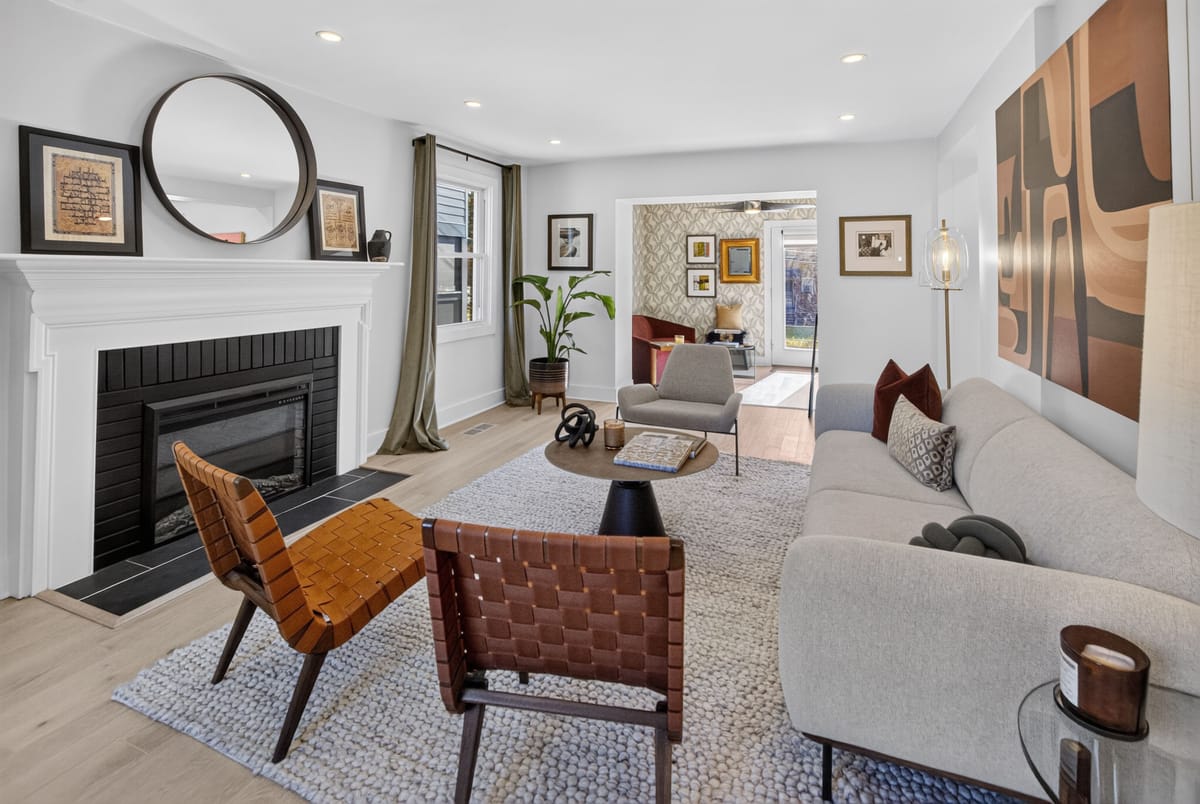 Living room with a cream sofa, two woven leather sling chairs and a large rust and umber abstract canvas above a black-tiled fireplace.