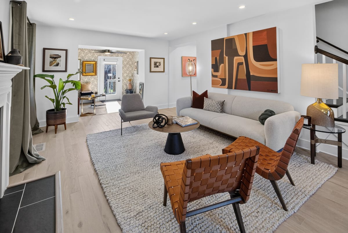 The finished living floor with a long cream sofa, woven leather sling chairs, a patterned rug and a large rust and orange canvas leading through to the dining room.
