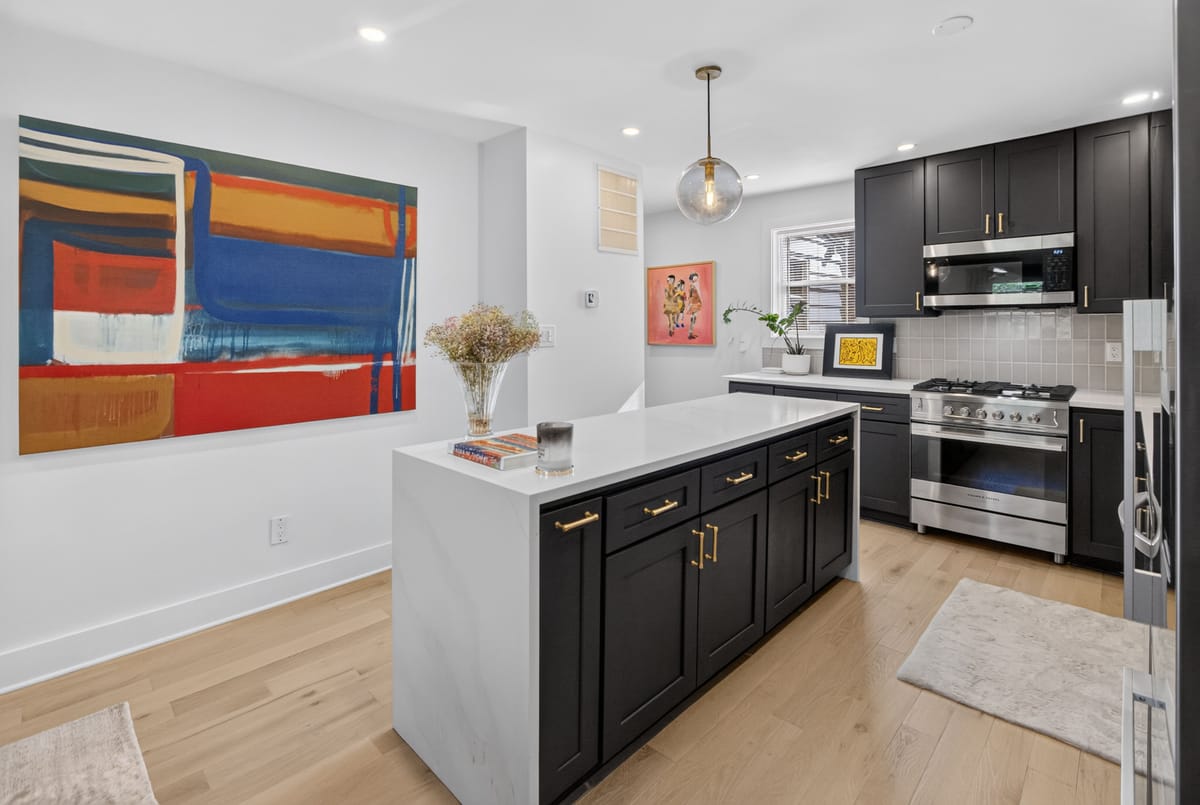 Kitchen seen past a bold red, blue and orange abstract canvas, with black cabinetry, a stainless range and a stone-topped island.