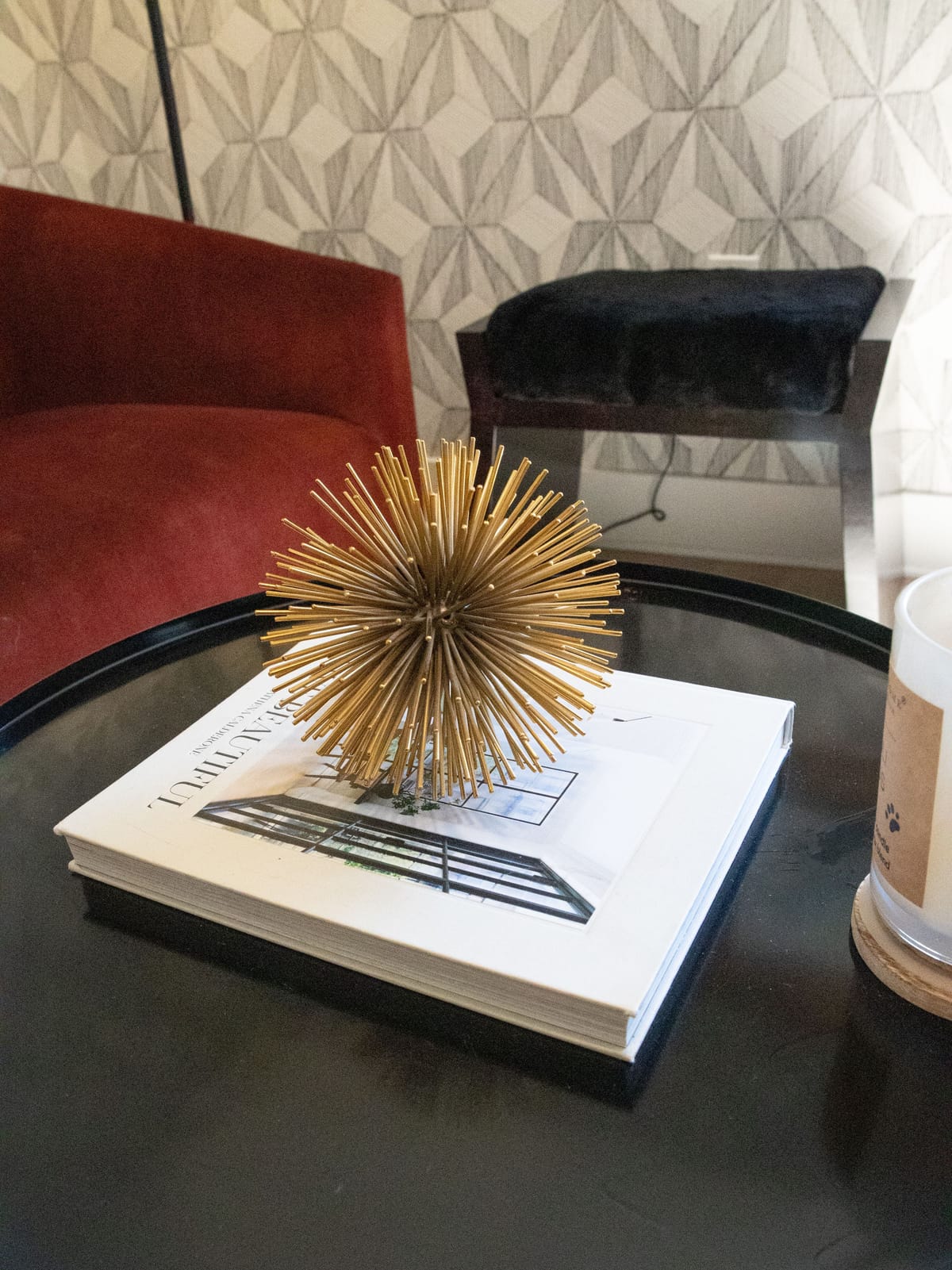 Detail of a red velvet chair beside a dark round table holding an open book and a small gold sculpture.