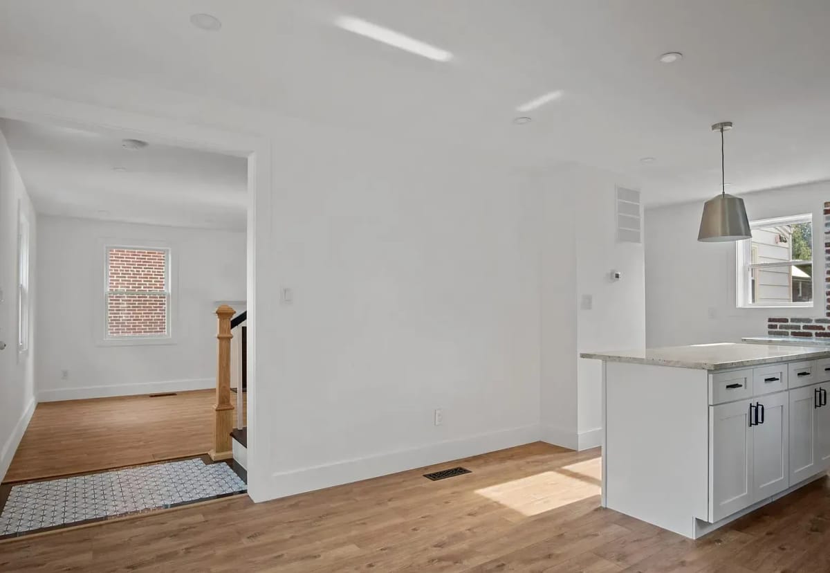 The kitchen and dining area empty, with white cabinetry, a stone-topped island and light oak floors.