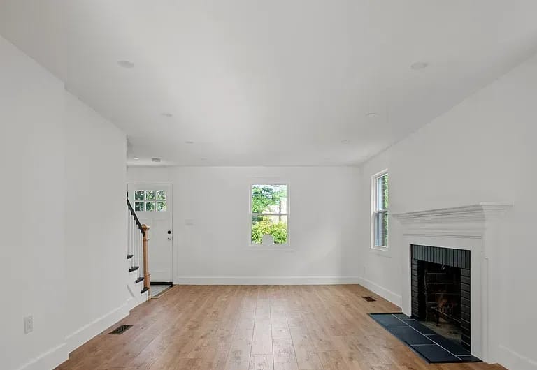 The living floor empty, with a stair rising at the left, a small window in the centre and the fireplace at the right.