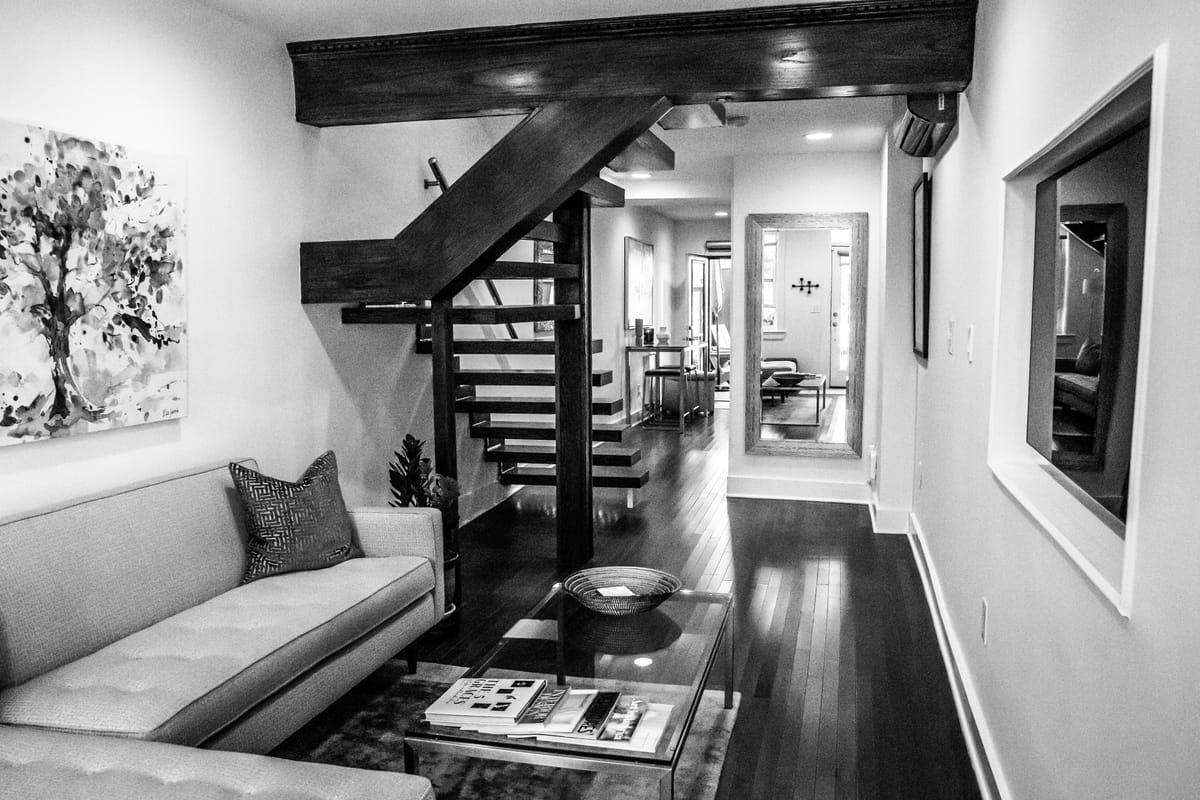 Black and white view of a front room with a tufted sofa, a low console and a sculptural black stair rising behind it.