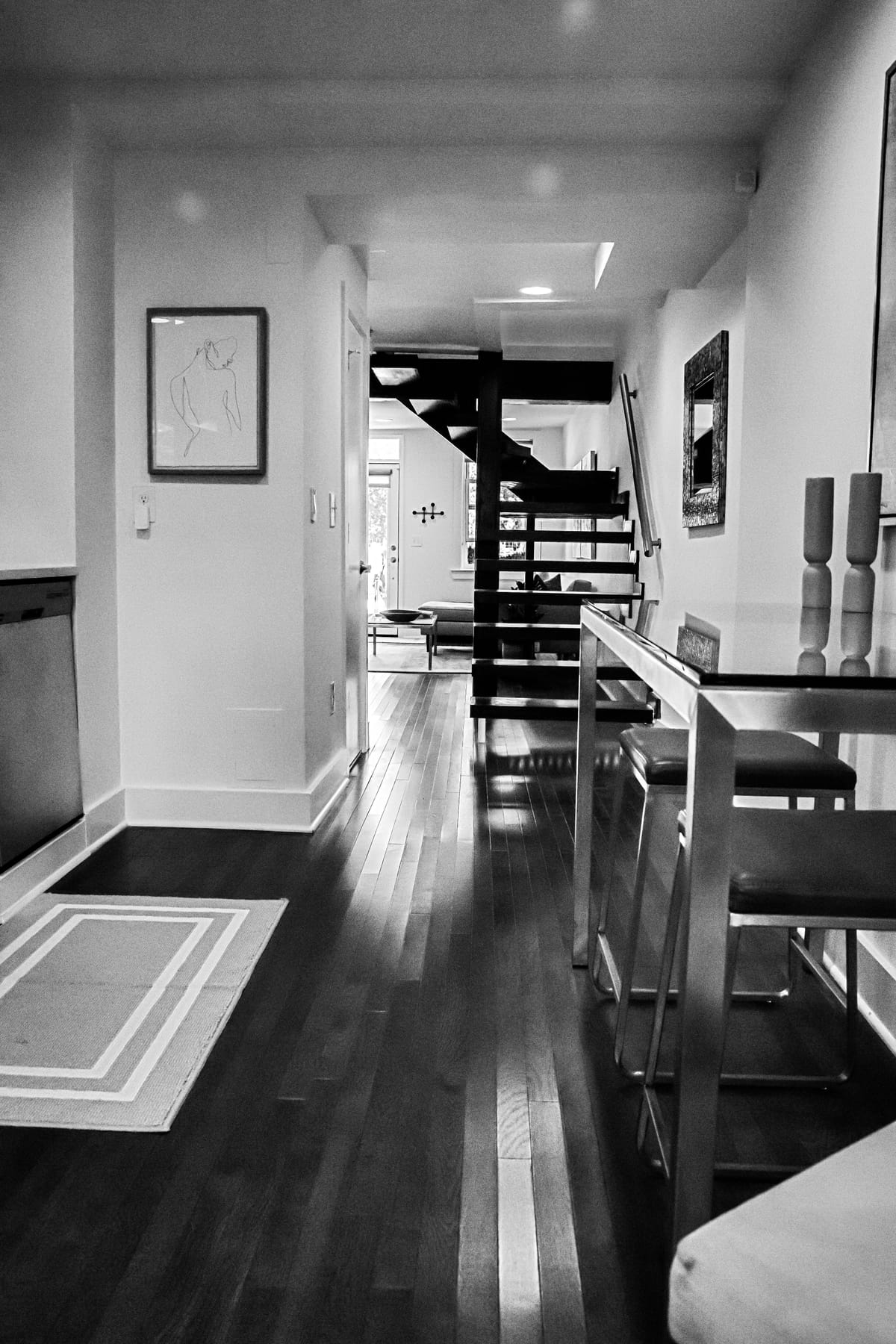 The reworked passage in black and white, with dark floors, a slim open stair and a mirrored wall carrying light down the plan.