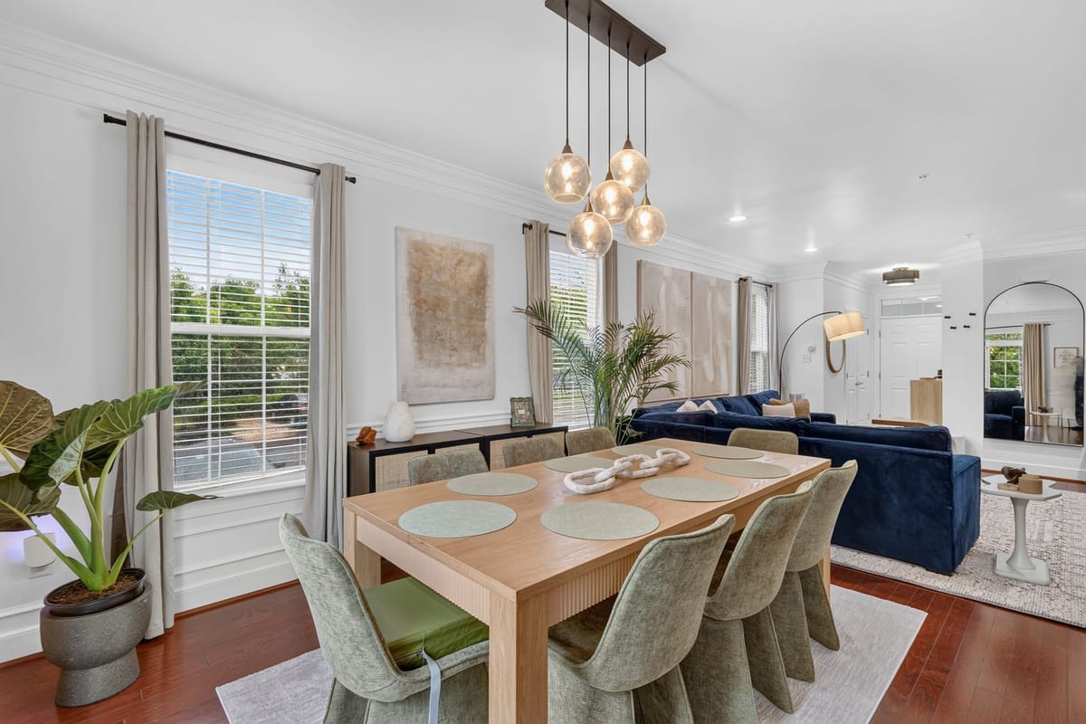 Open dining and living room with a pale oak table, green upholstered chairs, a navy velvet sectional and a cluster of glass pendants.