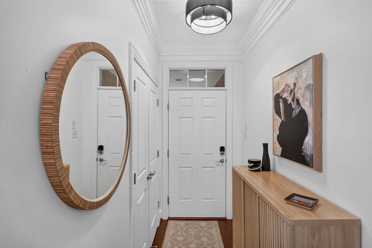 The finished entry with a round rattan mirror, a fluted oak console, a dark vase and a framed family portrait beside the front door.