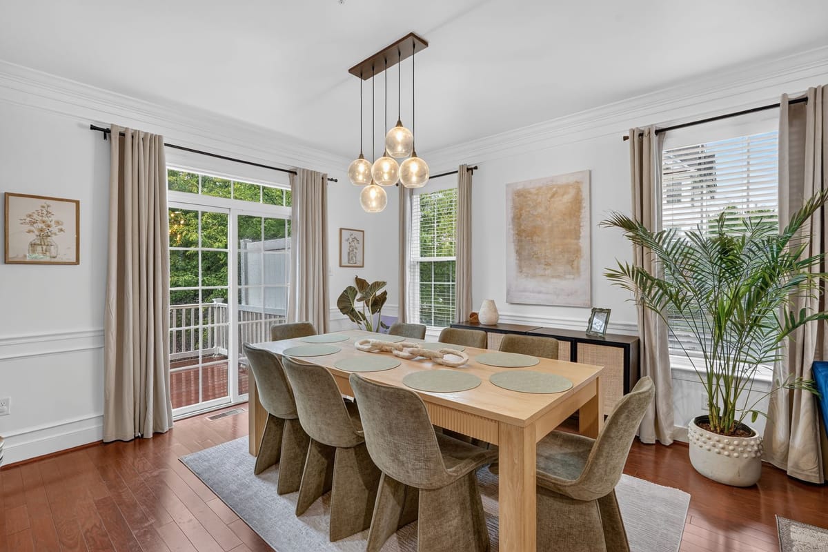 The finished dining bay with a pale oak table, sculptural boucle chairs, a linear glass pendant and a tall palm beside the garden doors.