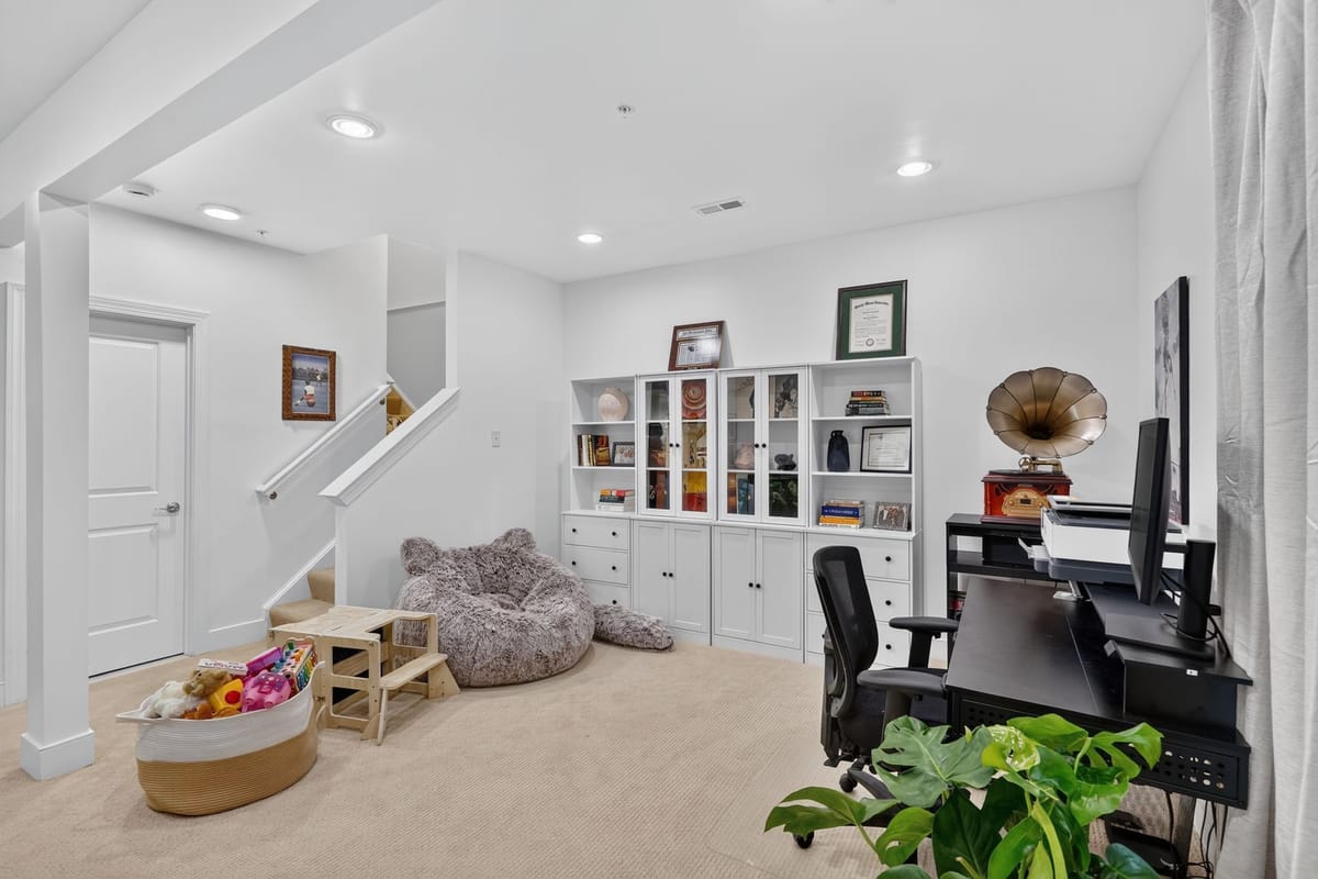 The finished lower level with a white built-in wall of shelving, a desk and monitors at one end and a soft play area at the other.