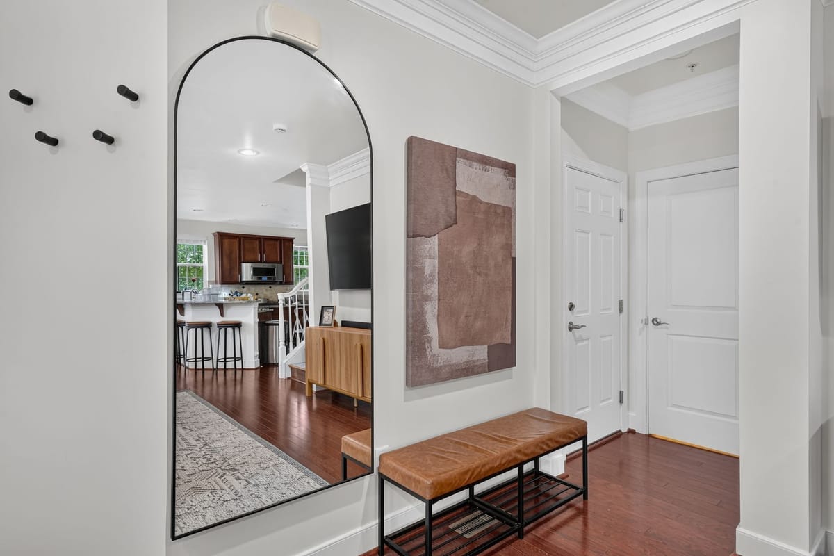 Entry vignette with a tall arched mirror reflecting the kitchen, a leather bench and a soft abstract canvas in clay tones.