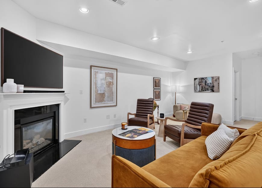 The basement lounge with a mustard sofa, two leather armchairs, a round tray table and a wall-mounted screen above the fireplace.