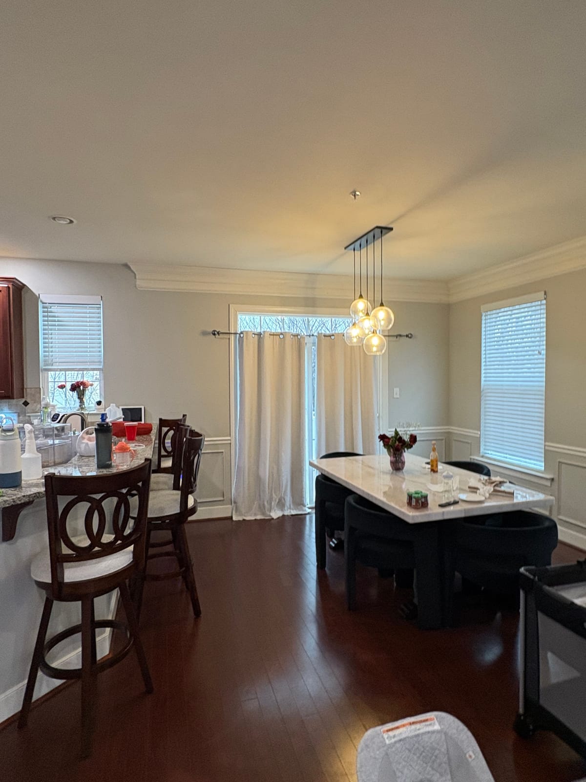 The dining area as found, seen past the kitchen counter, with a dark table and mismatched chairs under a small chandelier.
