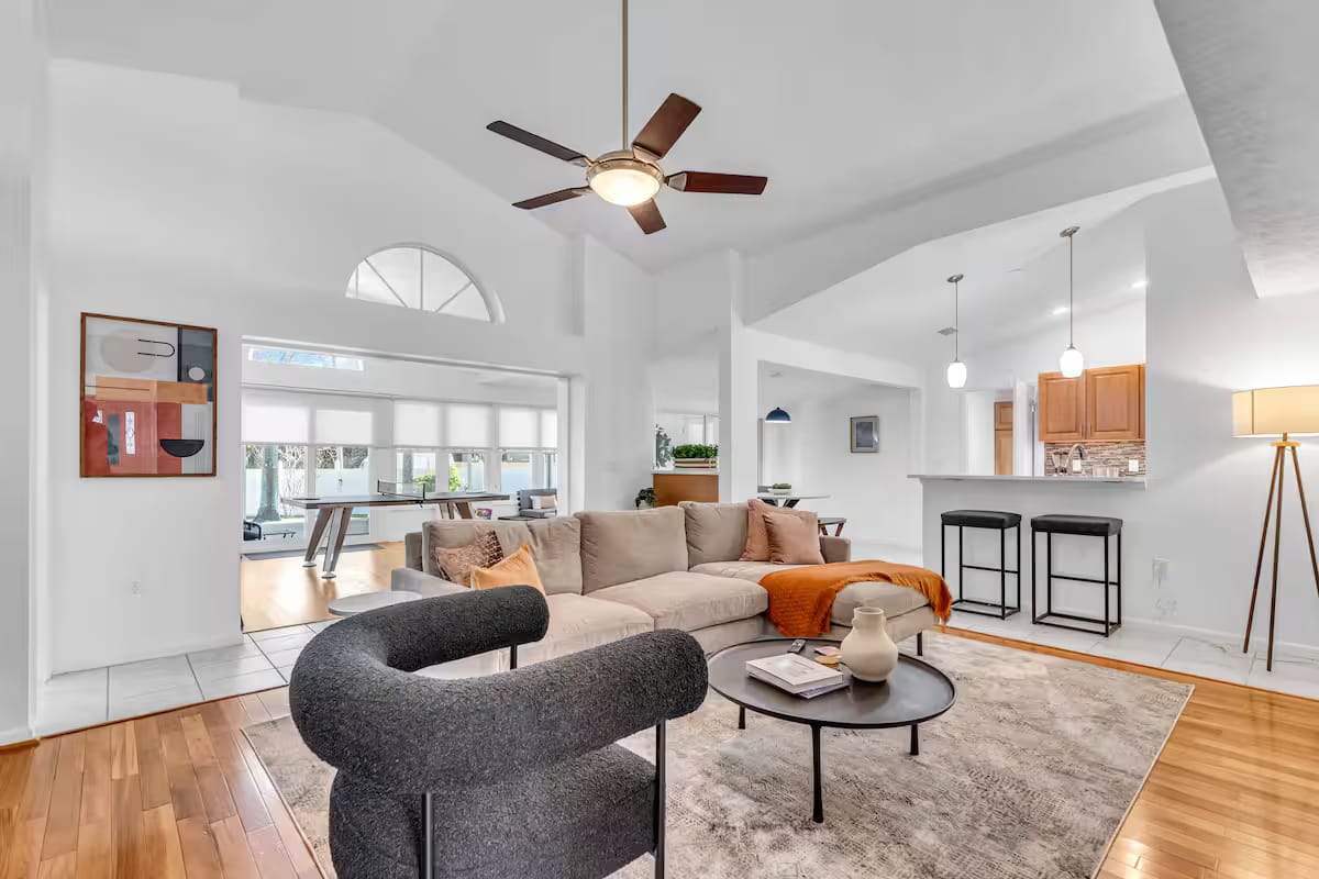 Vaulted great room with a cream sectional, a sculptural charcoal curved chair, a round black coffee table and an arched window wall.