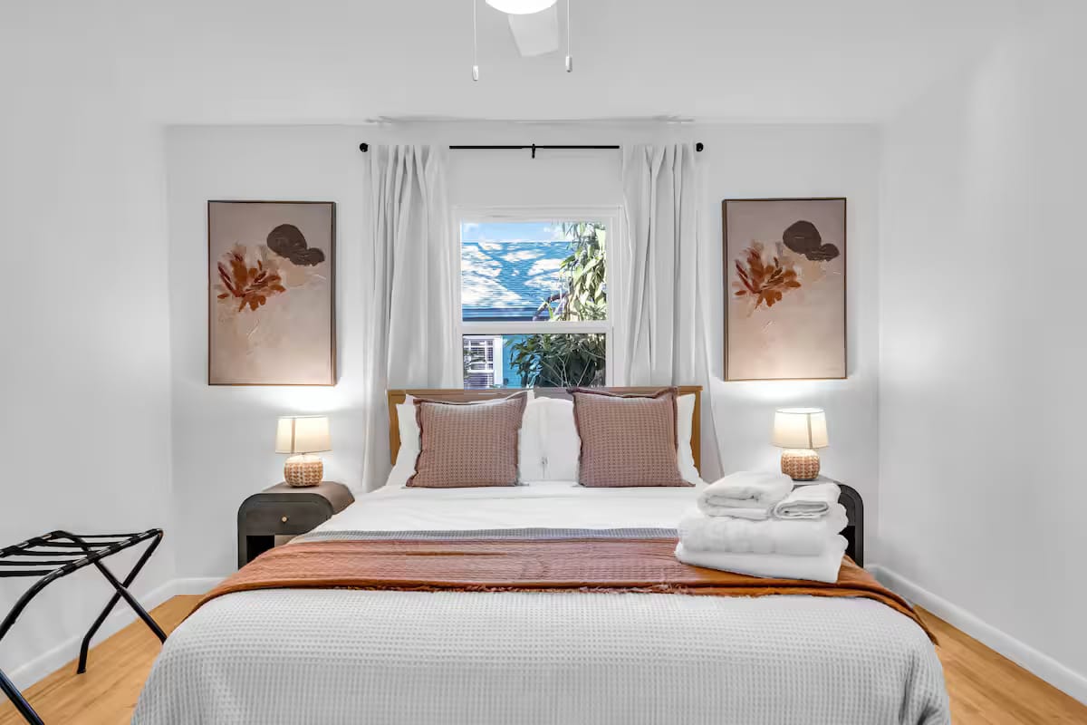 Bedroom with a low upholstered bed between two lamp-topped nightstands and a matched pair of botanical prints in clay tones.