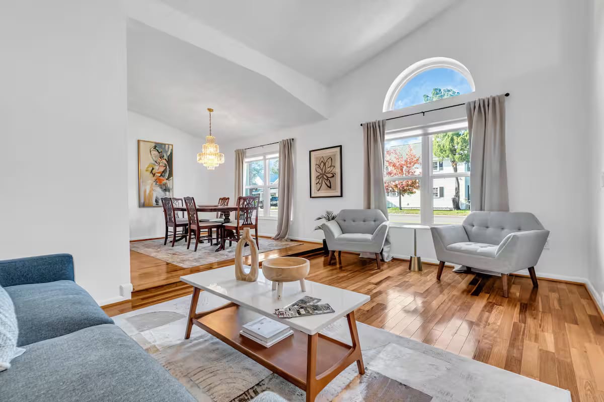 A second finished sitting area with a pale blue sofa, mid-century armchairs, a marble-topped coffee table and a round dining table beyond.