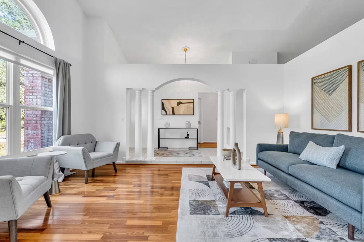 The finished living room with a slate-blue sofa, pale armchairs, a low timber coffee table and an arched window flooding the oak floor with light.
